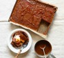 Sticky toffee pudding in a baking tray, with a separate bowlful alongside topped with ice cream and sauce